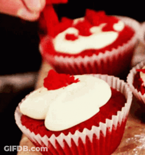 A Red Velvet Cupcake With White Frosting And A Red Strawberry On Top GIF