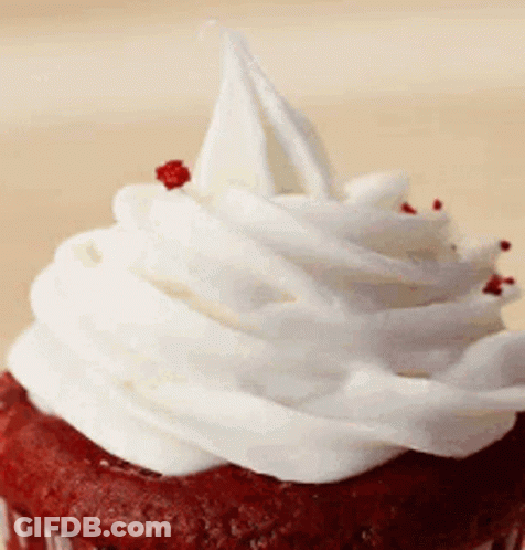 A Red Velvet Cupcake With White Frosting On Top GIF