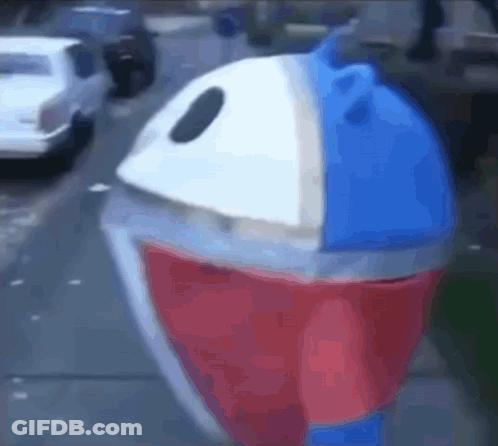 A Red , White And Blue Trash Can Is Sitting On The Side Of A Street . GIF