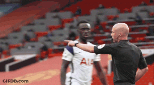 A Referee Is Pointing At A Soccer Player Who Is Wearing A Tottenham Shirt GIF