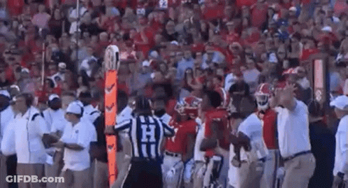 A Referee Is Standing In The Middle Of A Football Field Surrounded By Players And Coaches During A Game . GIF
