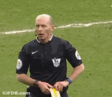 A Referee Is Standing On A Soccer Field Holding A Yellow Flag . GIF