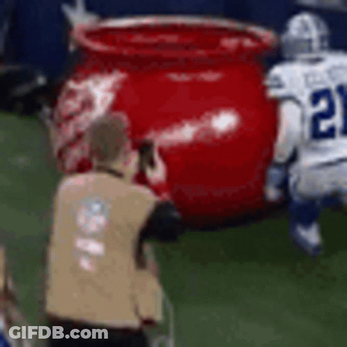 A Referee Is Taking A Picture Of A Football Player And A Large Red Pot On The Field . GIF
