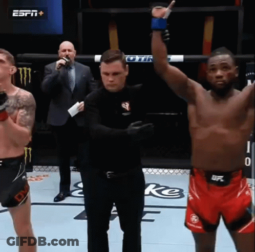 A Referee Stands Between Two Fighters In A Boxing Ring While One Of Them Raises His Hand In The Air GIF