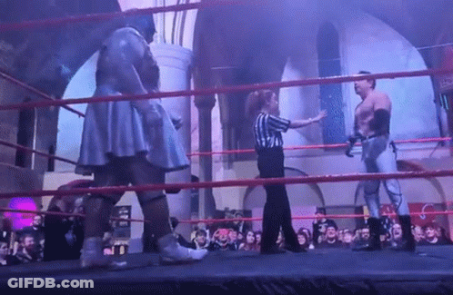 A Referee Stands In A Ring With Two Wrestlers GIF