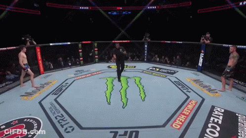 A Referee Stands In The Middle Of A UFC Ring With Monster Energy On The Floor GIF