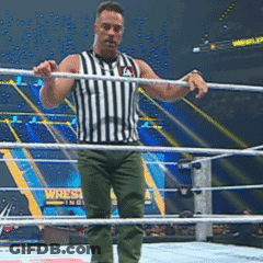 A Referee Stands In The Middle Of A Wrestling Ring With A Wrestlemania Sign In The Background GIF