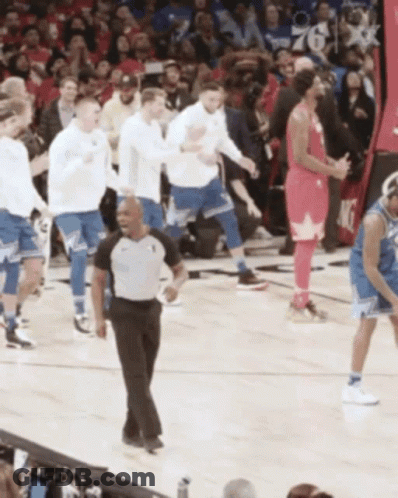A Referee Stands On A Basketball Court Surrounded By Basketball Players GIF