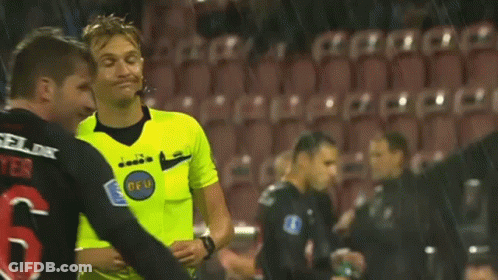 A Referee Wearing A Yellow Shirt With The Word Diadora On It Is Standing On A Soccer Field . GIF