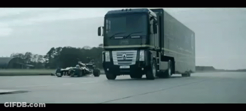 A Renault Truck Is Driving Down A Road With A Race Car Behind It GIF