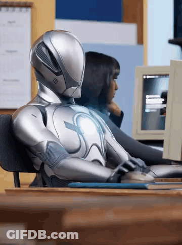 A Robot Is Sitting At A Desk Using A Computer GIF