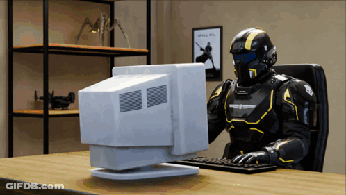 A Robot Is Sitting At A Desk Using A Computer With A Poster On The Wall That Says Spill On GIF