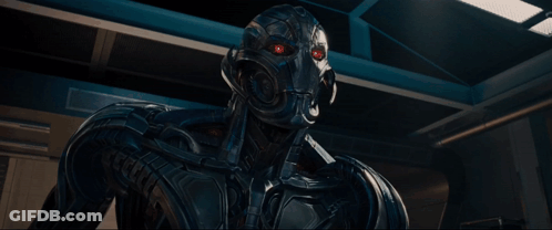 A Robot Is Standing In A Dark Room With A Blue Light Behind Him GIF