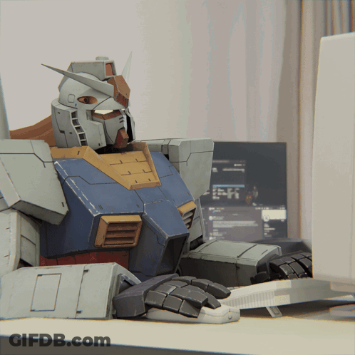 A Robot Sits At A Desk In Front Of A Computer Screen GIF
