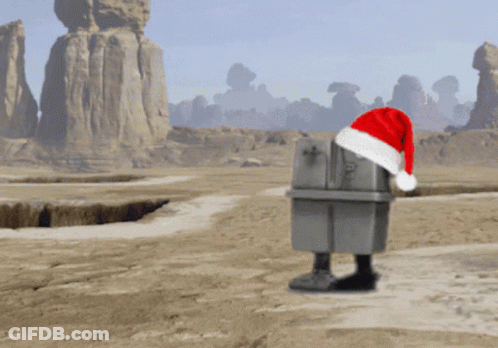 A Robot Wearing A Santa Hat Stands In A Desert GIF