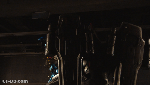 A Robot With A Glowing Blue Armor Is Standing Next To A Large Shield GIF