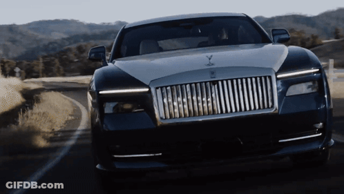 A Rolls Royce Car Is Driving Down A Road With Mountains In The Background GIF