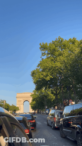 A Row Of Cars Are Parked On A Street In Front Of A Large Archway GIF
