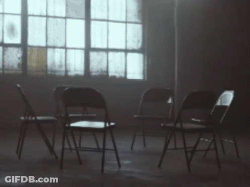 A Row Of Folding Chairs In A Dark Room With A Window In The Background GIF