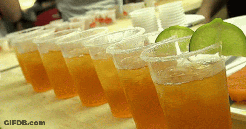 A Row Of Plastic Cups Filled With Orange Liquid And Lime Slices On A Table GIF