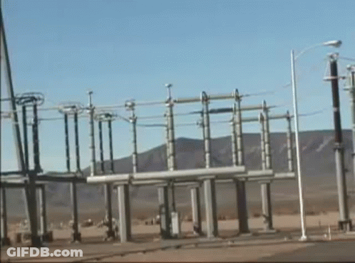 A Row Of Power Lines In A Field With Mountains In The Background . GIF