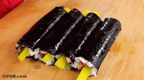 A Row Of Sushi Rolls With Yellow Onions On A Wooden Table GIF