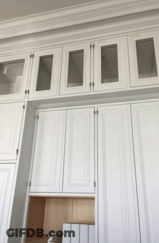 A Row Of White Cabinets With Glass Doors On Top GIF