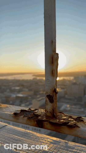 A Rusty Railing With A City In The Background At Sunset GIF