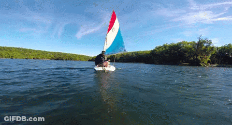 A Sailboat With A Red White And Blue Sail Is Floating On The Water GIF