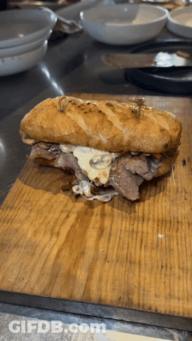 A Sandwich Is On A Wooden Cutting Board On A Table GIF