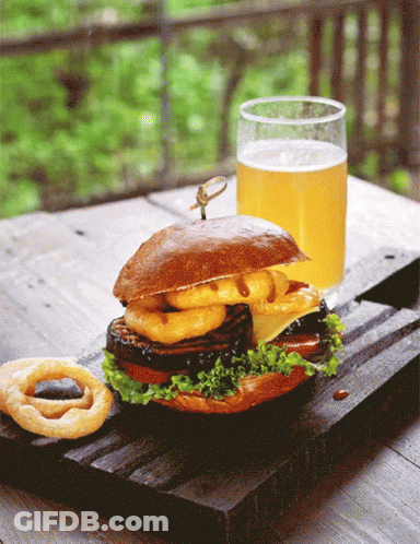 A Sandwich With Onion Rings And A Glass Of Beer On A Wooden Table GIF