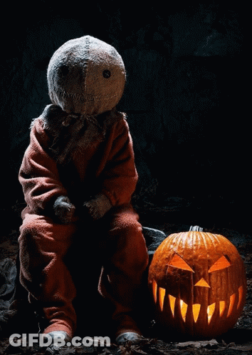 A Scarecrow Sits Next To A Carved Pumpkin That Is Lit Up GIF