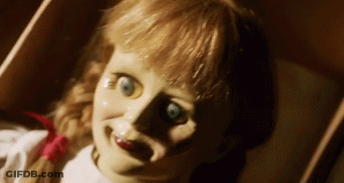 A Scary Doll Is Laying In A Box And Smiling At The Camera . GIF