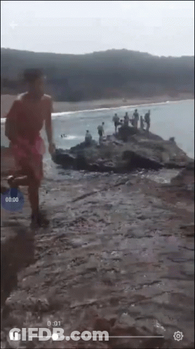 A Screenshot Of A Video Of People On A Rocky Beach With The Time Of 0:01 GIF