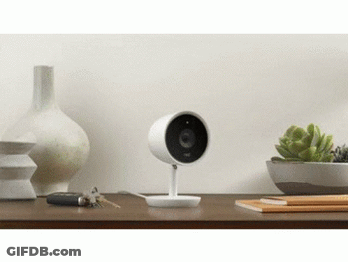 A Security Camera Is Sitting On Top Of A Wooden Table Next To A Vase And Keys . GIF