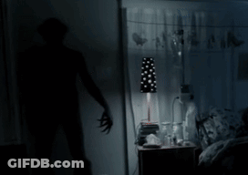A Shadow Of A Person Standing In A Dark Room With A Lamp GIF