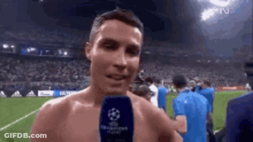 A Shirtless Athlete Is Talking Into A Microphone On A Soccer Field . GIF