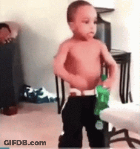 A Shirtless Baby Is Standing In A Living Room Holding A Green Bottle Of Water . GIF