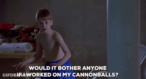 A Shirtless Boy In Blue Shorts Is Standing In A Dark Room And Talking To Someone . GIF