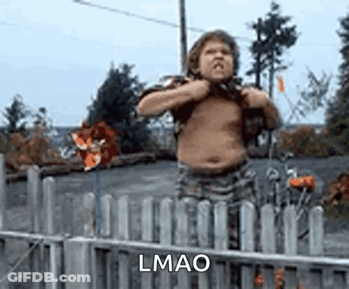 A Shirtless Boy Is Standing In Front Of A Fence And Holding His Chest . GIF