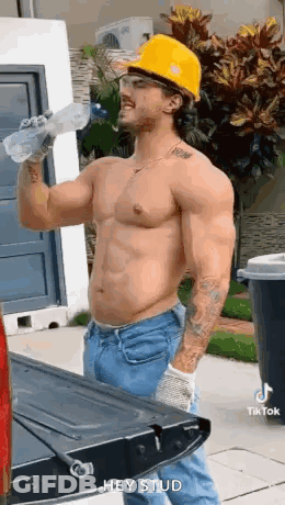 A Shirtless Construction Worker Is Drinking Water From A Bottle While Standing Next To A Truck . GIF