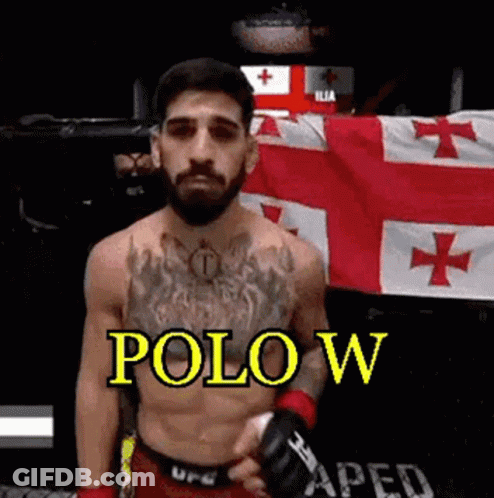 A Shirtless Fighter With A Beard Is Standing In Front Of A Flag And Holding A Glove . GIF