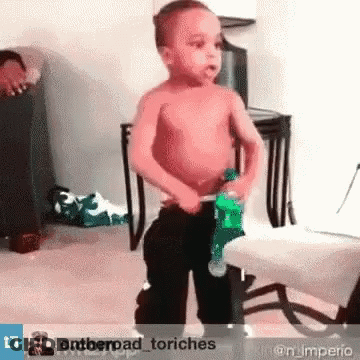 A Shirtless Little Boy Is Holding A Green Bottle In His Hand GIF