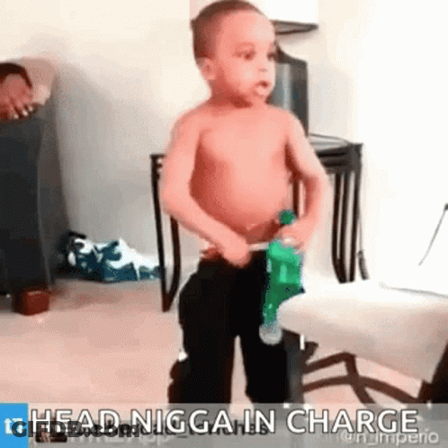 A Shirtless Little Boy Is Standing Next To A Chair And Holding A Bottle Of Water . GIF