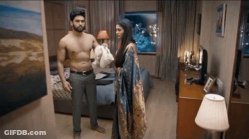 A Shirtless Man And A Woman Are Standing In A Bedroom GIF