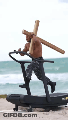 A Shirtless Man Carrying A Wooden Cross On A Treadmill On The Beach GIF