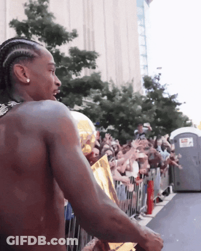 A Shirtless Man Holds A Trophy In Front Of A Crowd Of People GIF