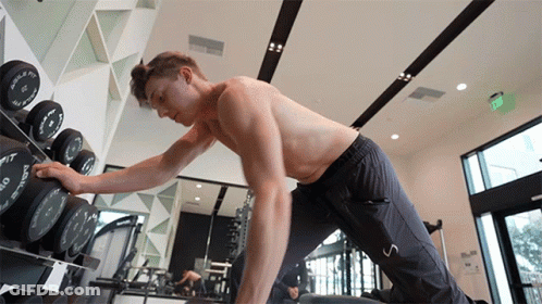 A Shirtless Man In A Gym Reaches For A Dumbbell That Says O'neill On It GIF