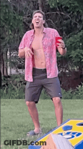 A Shirtless Man In A Pink Shirt Is Holding A Red Cup While Standing Next To A Cornhole Board . GIF