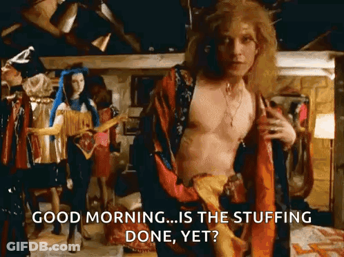 A Shirtless Man In A Robe Is Standing In A Room With A Woman Standing Behind Him . GIF